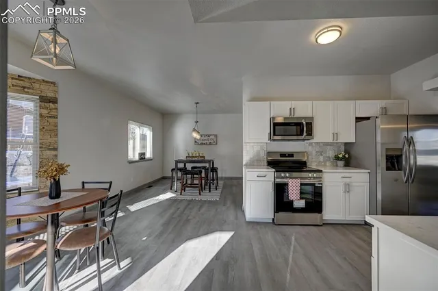 a kitchen with stainless steel appliances granite countertop a stove top oven a sink dishwasher a dining table and chairs with wooden floor