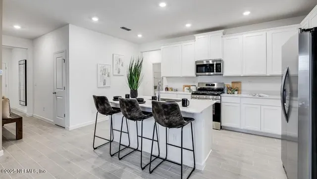 a kitchen with stainless steel appliances a microwave a stove a sink a refrigerator and white cabinets with wooden floor