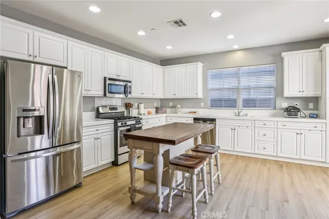 a kitchen with stainless steel appliances granite countertop a refrigerator a sink dishwasher a stove and white cabinets with wooden floor