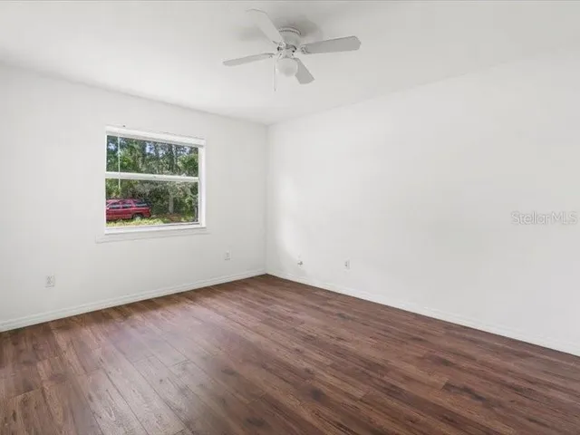 an empty room with wooden floor ceiling fan and windows