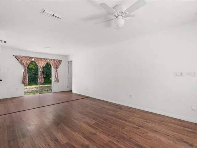 an empty room with wooden floor fan and windows