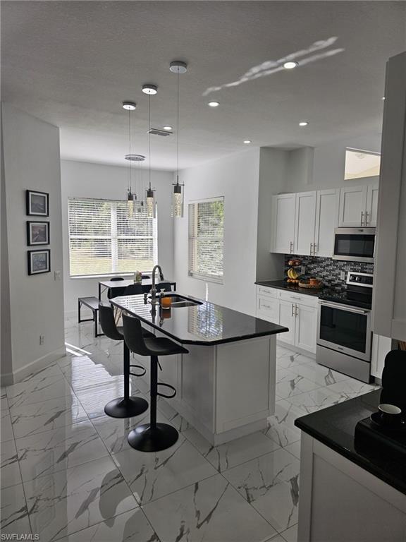 4340 Golden Gate Boulevard East Naples, FL 34120 - Photo 3 of 41 Kitchen featuring stainless steel appliances, white cabinetry, pendant lighting, tasteful backsplash, and a kitchen breakfast bar