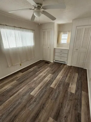 an empty room with wooden floor fan and windows