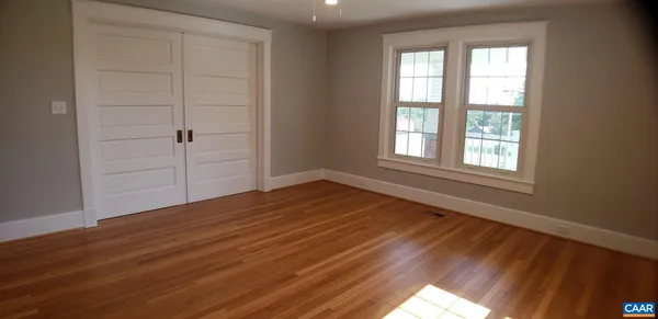 a view of an empty room with wooden floor and a window