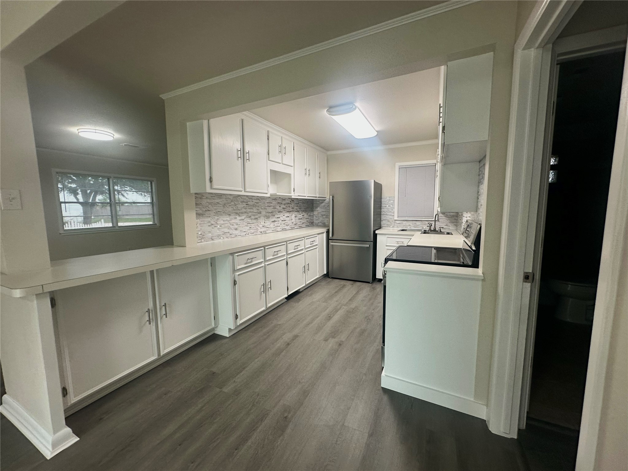 130 Bay Ridge Drive Baytown, TX 77523 - Photo 9 of 20 This photo showcases a bright, modern kitchen with sleek white cabinetry, a stainless steel refrigerator, and a stylish tile backsplash. The room features ample counter space and wood-style flooring, creating a contemporary and inviting atmosphere.