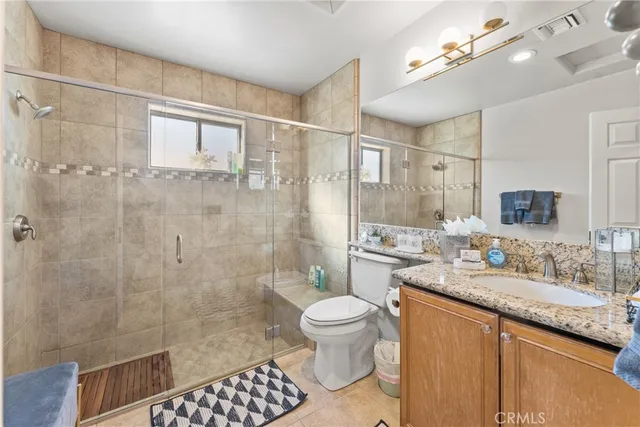 a bathroom with a granite countertop sink a toilet a mirror and shower