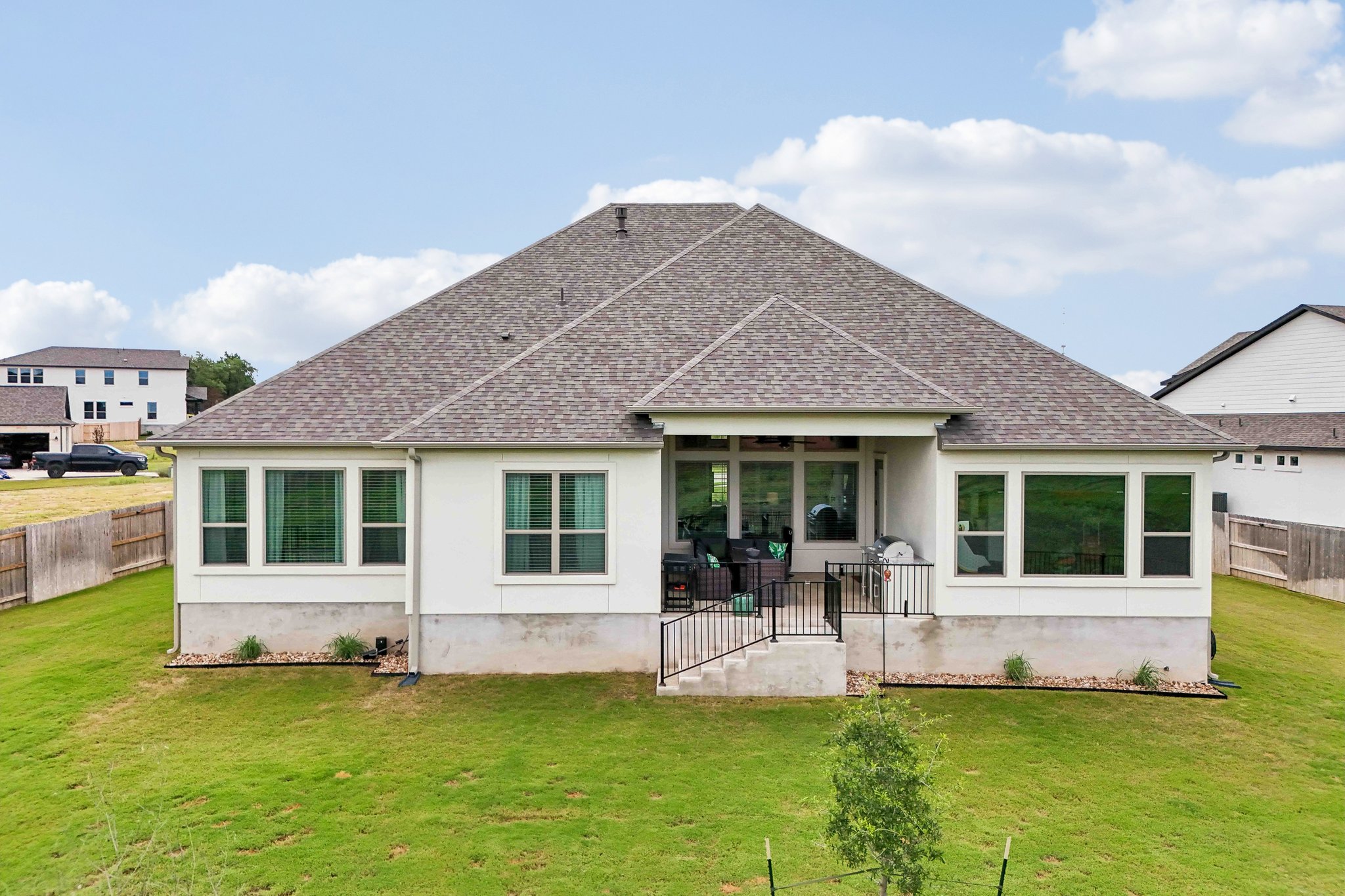 130 Firethorn Loop Bastrop, TX 78602 - Photo 29 of 38 Rear exterior featuring a covered patio, multiple large windows, and a sloped backyard with a wooden fence boundary