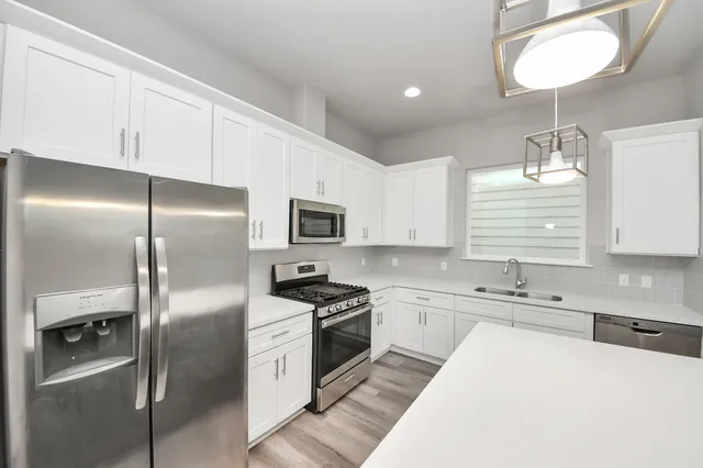 a kitchen with stainless steel appliances granite countertop a refrigerator a sink a stove and white cabinets