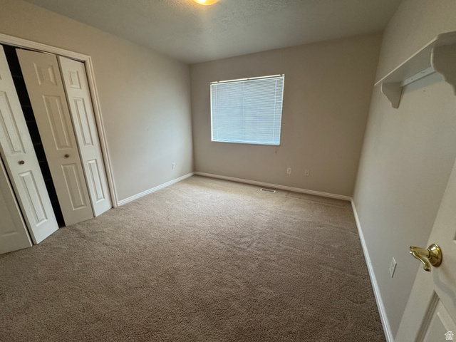 88 Canterbury Lane Logan, UT 84321 - Photo 23 of 37 Carpeted room featuring a window with blinds, bi-fold closet doors, wall-mounted shelving, and a brass door handle