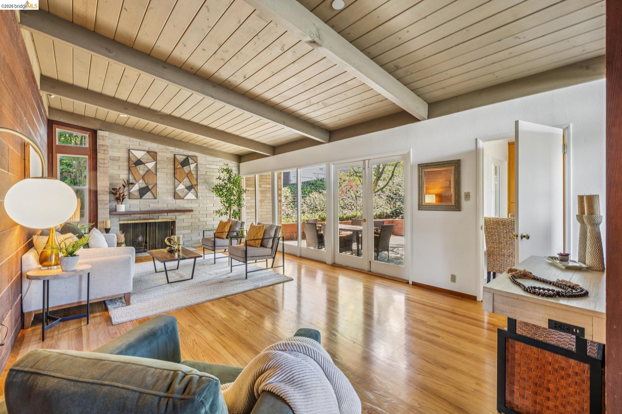 1024 Overlook Road Berkeley, CA 94708 - Photo 14 of 41 Vaulted ceiling with exposed beams, wood-finish flooring, stone-clad fireplace with mantel, French doors, and wood accent wall