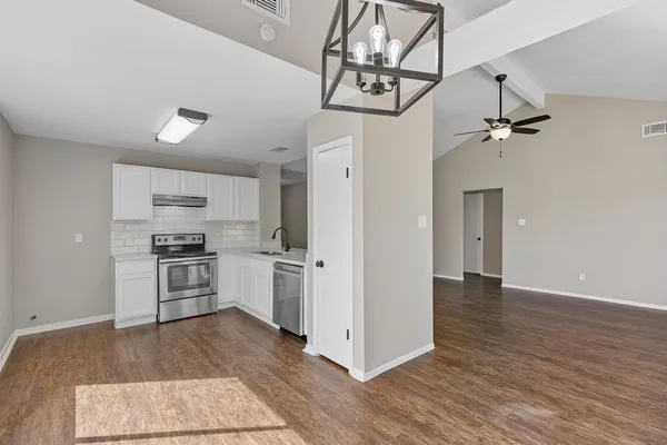 a kitchen with stainless steel appliances granite countertop a refrigerator a stove a sink and white cabinets with wooden floor