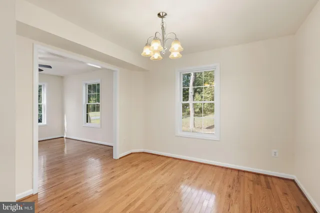 an empty room with wooden floor chandelier and windows