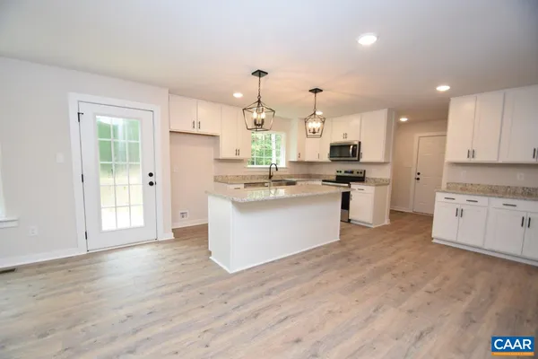 a large kitchen with stainless steel appliances kitchen island granite countertop a stove a sink dishwasher and white cabinets with wooden floor