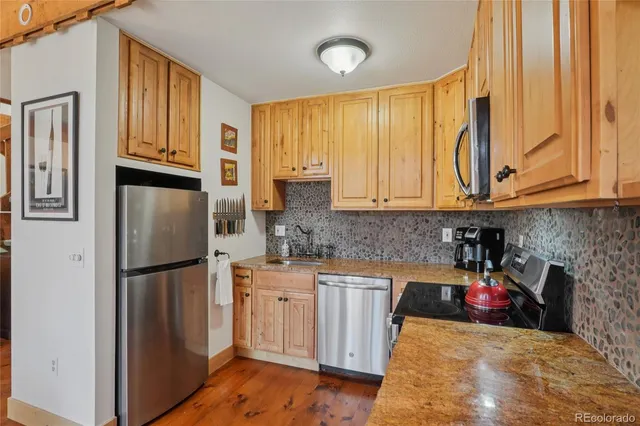 a kitchen with stainless steel appliances granite countertop a refrigerator a sink dishwasher and wooden cabinets with wooden floor