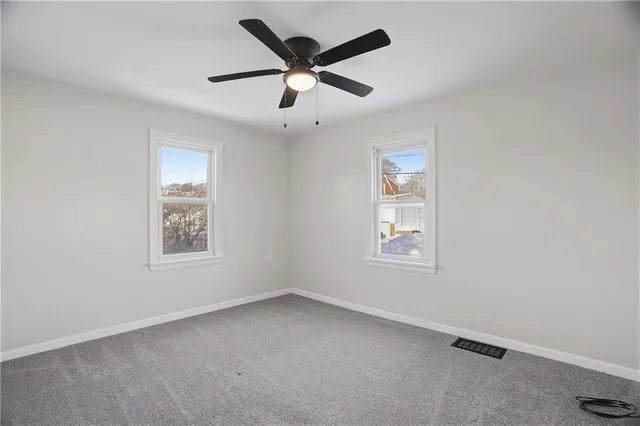 an empty room with ceiling fan and windows