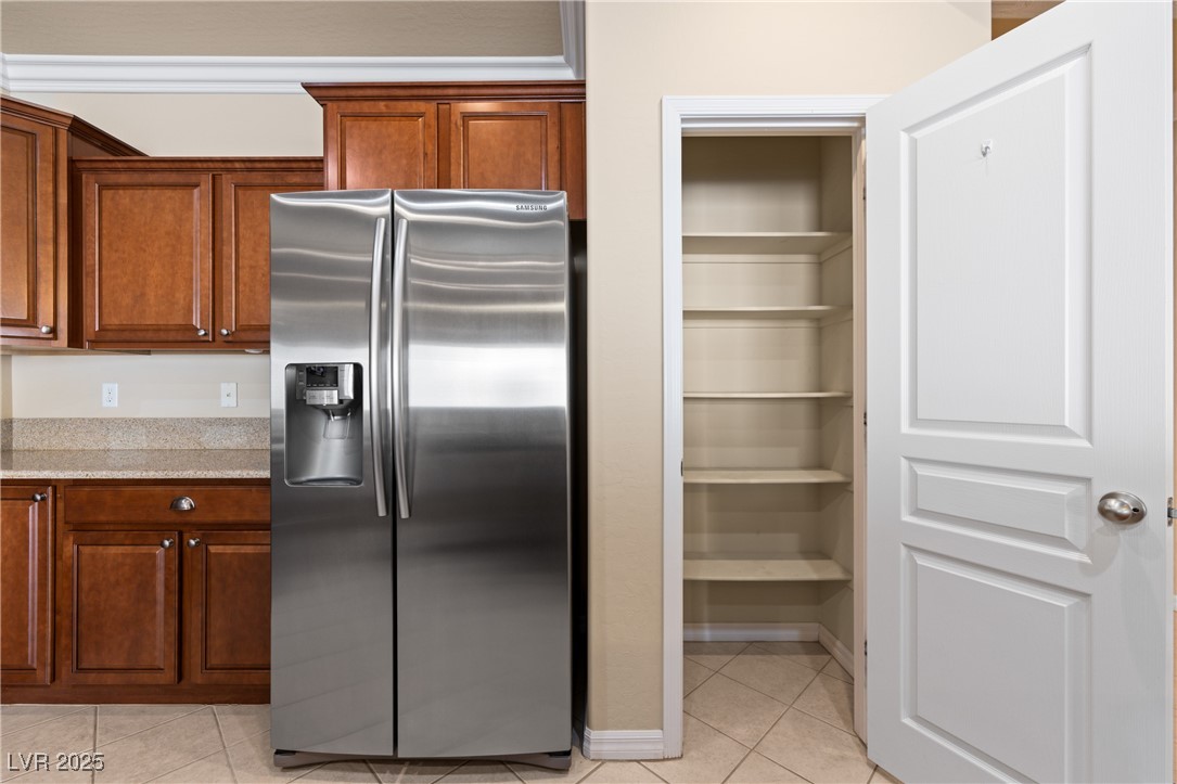 1551 Watchmans Point Mesquite, NV 89034 - Photo 28 of 62 Kitchen with stainless steel fridge with ice dispenser, light tile patterned flooring, light stone counters, and brown cabinetry