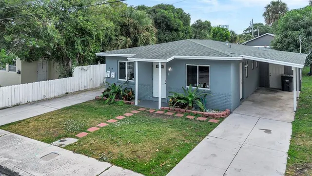 a view of a house with a yard plants and a large tree