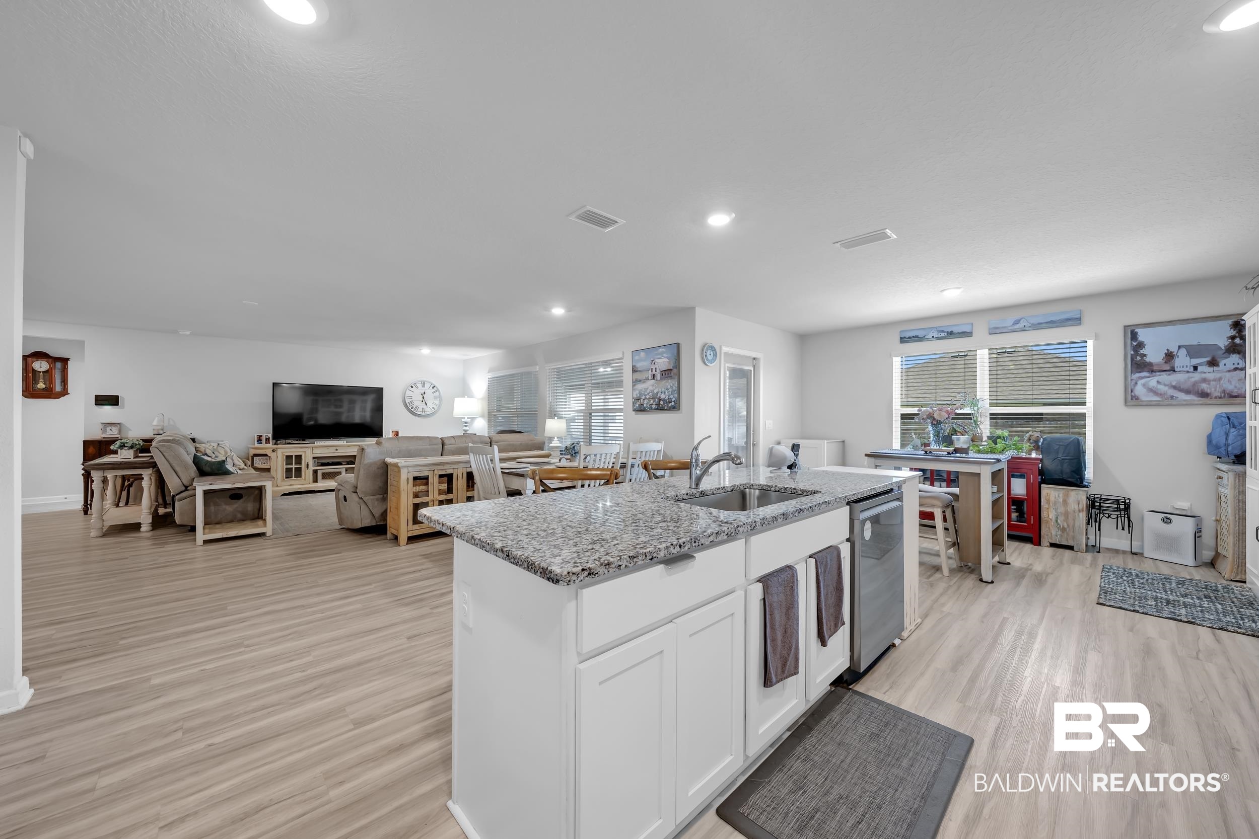 24271 Ringneck Loop Elberta, AL 36530 - Photo 14 of 44 Open-concept living space featuring wood-finish flooring throughout, a kitchen island with a double basin sink and stone-look countertop, white cabinetry, and recessed lighting