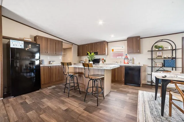 a kitchen with stainless steel appliances kitchen island granite countertop a refrigerator a stove a sink dishwasher and a dining table with wooden floor