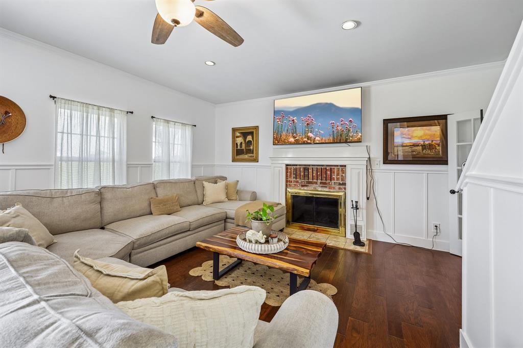 331 Radecke Road Krum, TX 76249 - Photo 8 of 40 Living area featuring rich wood-finish flooring, white wainscoting, and a brick fireplace with a white mantel