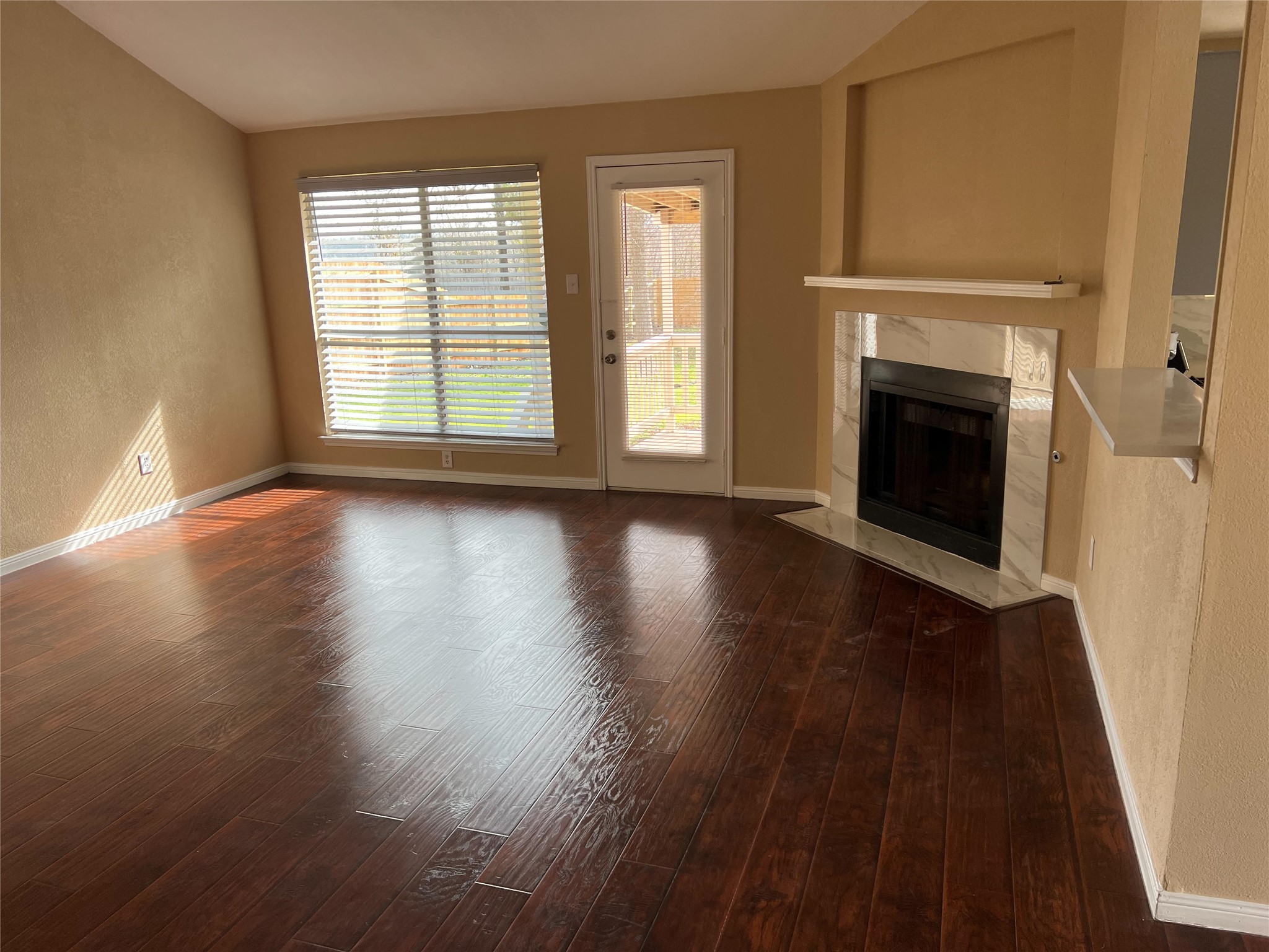 711 Pigeon Forge Road Pflugerville, TX 78660 - Photo 2 of 9 Unfurnished living room featuring a fireplace, baseboards, dark wood-style flooring, and a textured wall
