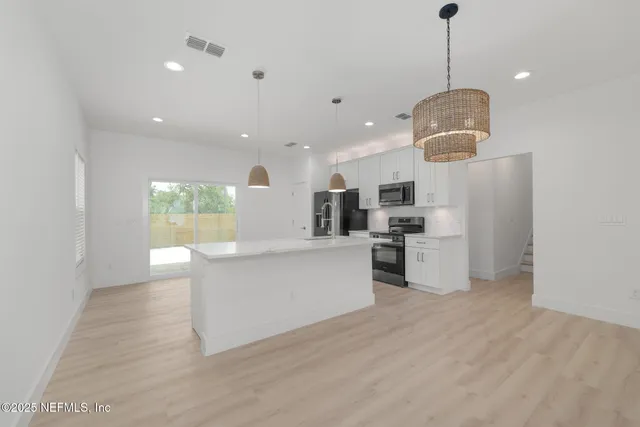 a kitchen with stainless steel appliances granite countertop a refrigerator a sink dishwasher a oven and a dining table with wooden floor