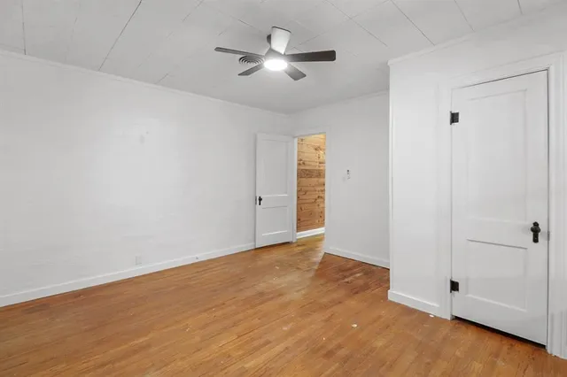 an empty room with a chandelier fan and wooden floor