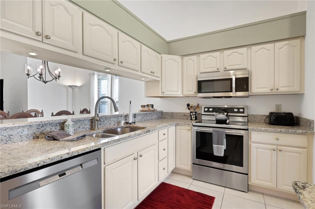 841 Kings Way Naples, FL 34104 - Photo 4 of 43 Kitchen featuring appliances with stainless steel finishes, light stone counters, light tile patterned floors, a chandelier, and white cabinetry