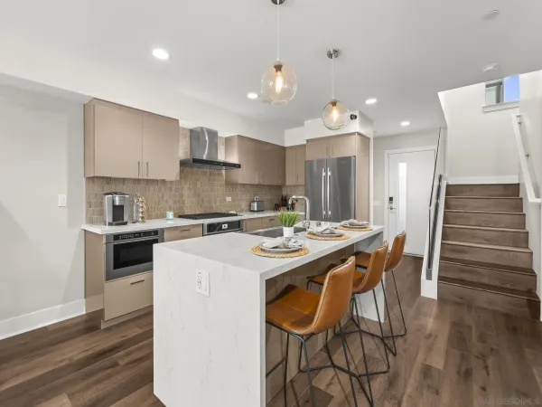 a kitchen with stainless steel appliances kitchen island granite countertop a stove a sink a refrigerator and white cabinets with wooden floor