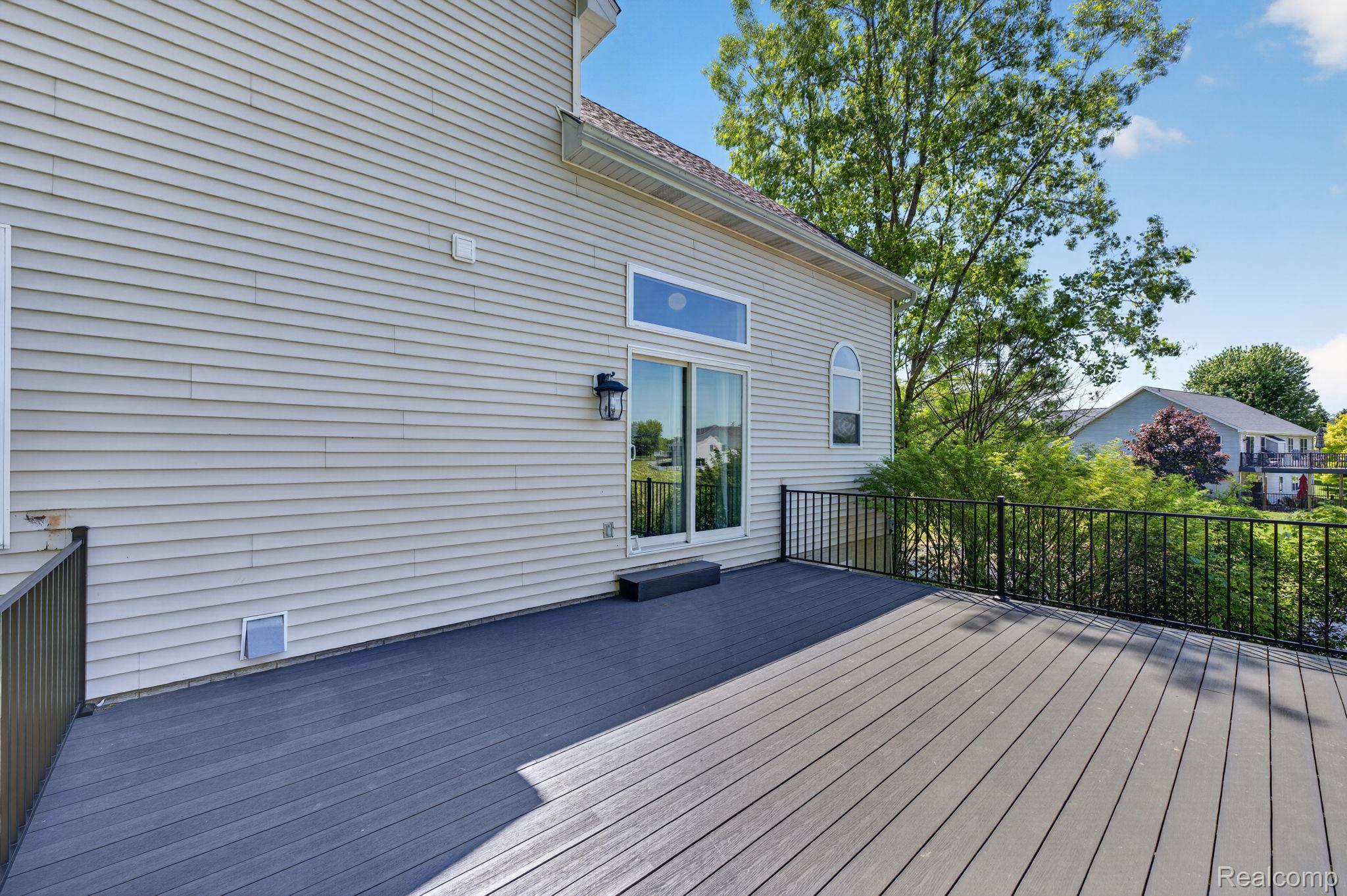 9055 Hegel Road Grand Blanc, MI 48439 - Photo 13 of 62 Spacious composite deck with dark gray surface and black metal railings, featuring light-colored siding and a sliding glass door with transom window