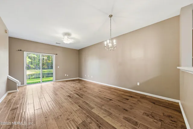 a view of an empty room with wooden floor fridge and a window