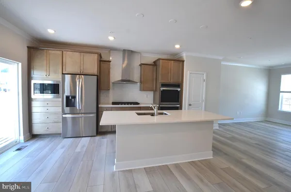 a large kitchen with stainless steel appliances a large counter top a stove a refrigerator with white cabinets and wooden floor