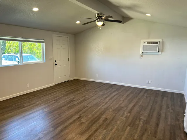 an empty room with wooden floor fan and windows