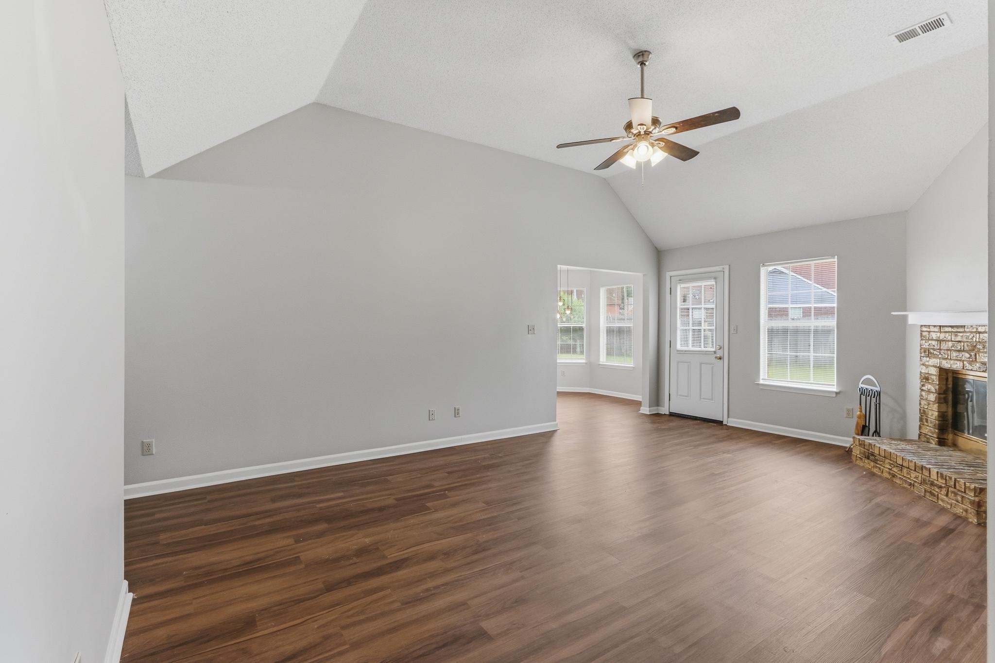 4101 Long Creek Road Memphis, TN 38125 - Photo 11 of 36 Spacious room featuring vaulted ceilings, wood-finish flooring, a ceiling fan with integrated lighting, and a brick fireplace