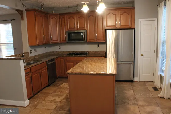 a kitchen with stainless steel appliances granite countertop a refrigerator a stove and a sink with wooden cabinets