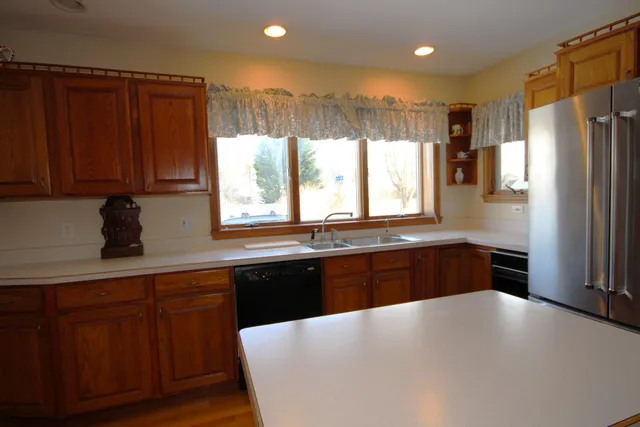 a kitchen with stainless steel appliances granite countertop a refrigerator a sink dishwasher and wooden cabinets with wooden floor