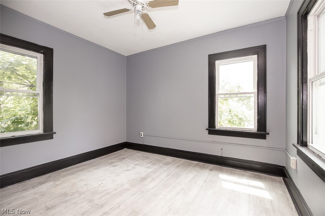 1868-1870 Lampson Road Cleveland, OH 44112 - Photo 17 of 36 Room featuring light wood-finish flooring, two large windows with dark trim, a ceiling fan, and light gray walls