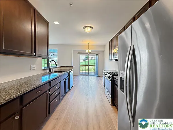 a kitchen with stainless steel appliances granite countertop a refrigerator a sink a stove and a wooden floors