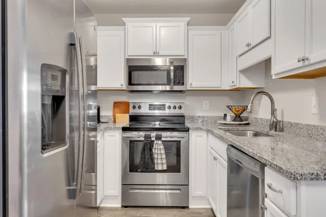 a kitchen with stainless steel appliances granite countertop a refrigerator a stove a sink and white cabinets