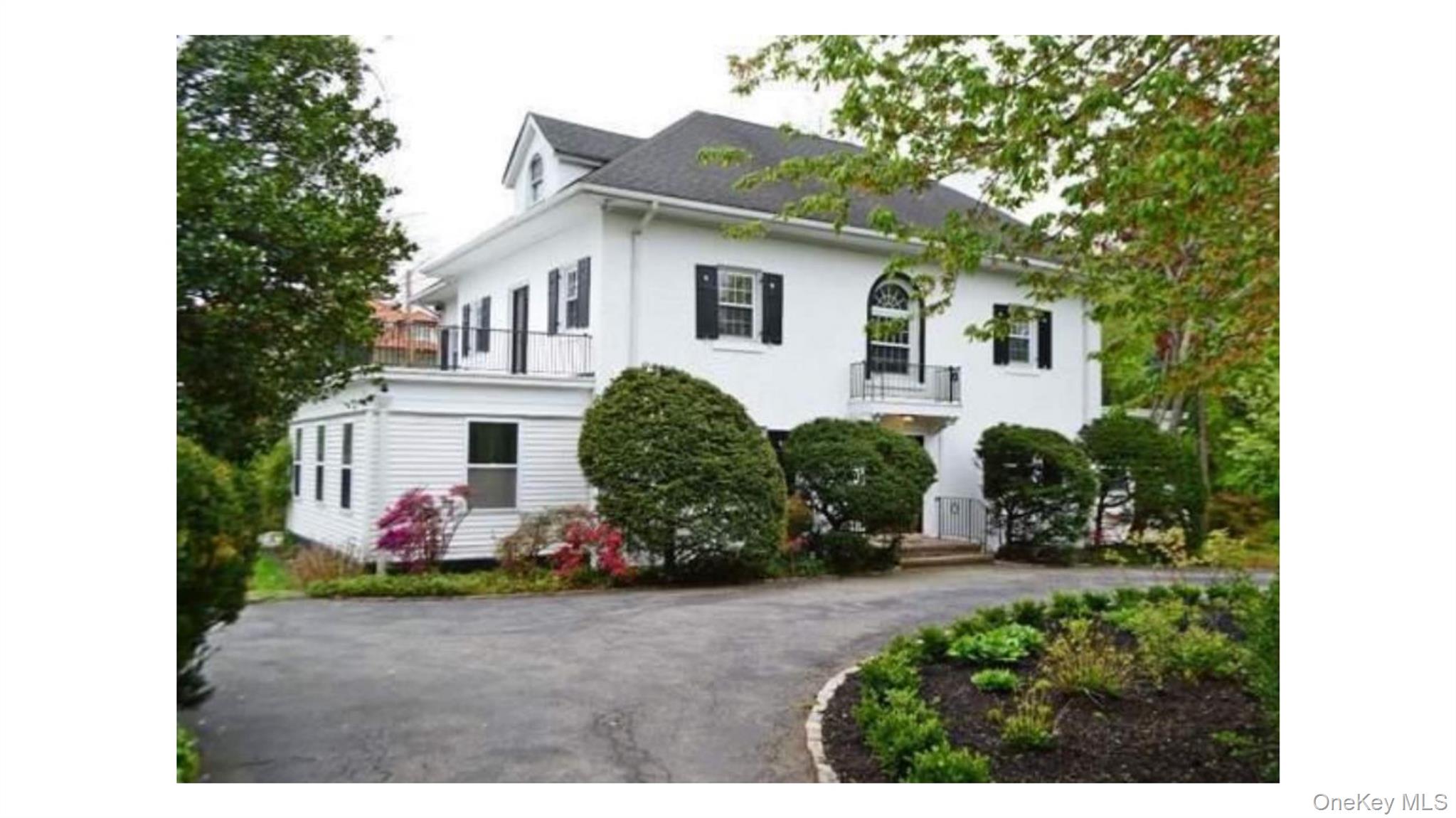 2 Arleigh Road Great Neck, NY 11021 - Photo 1 of 22 White exterior with black shutters, dormer window, second-story balcony with metal railing, and a paved driveway