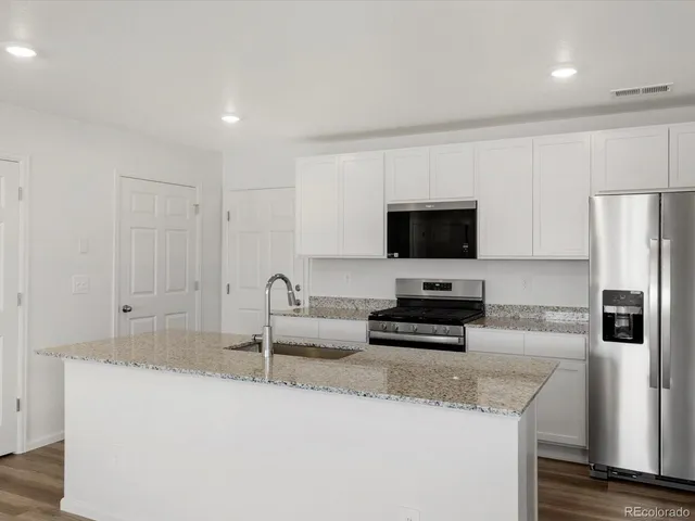 a kitchen with granite countertop a refrigerator a stove a microwave and island with wooden floor