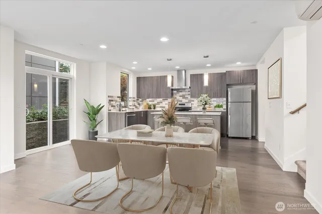 a dining room with stainless steel appliances kitchen island granite countertop a dining table chairs and a refrigerator