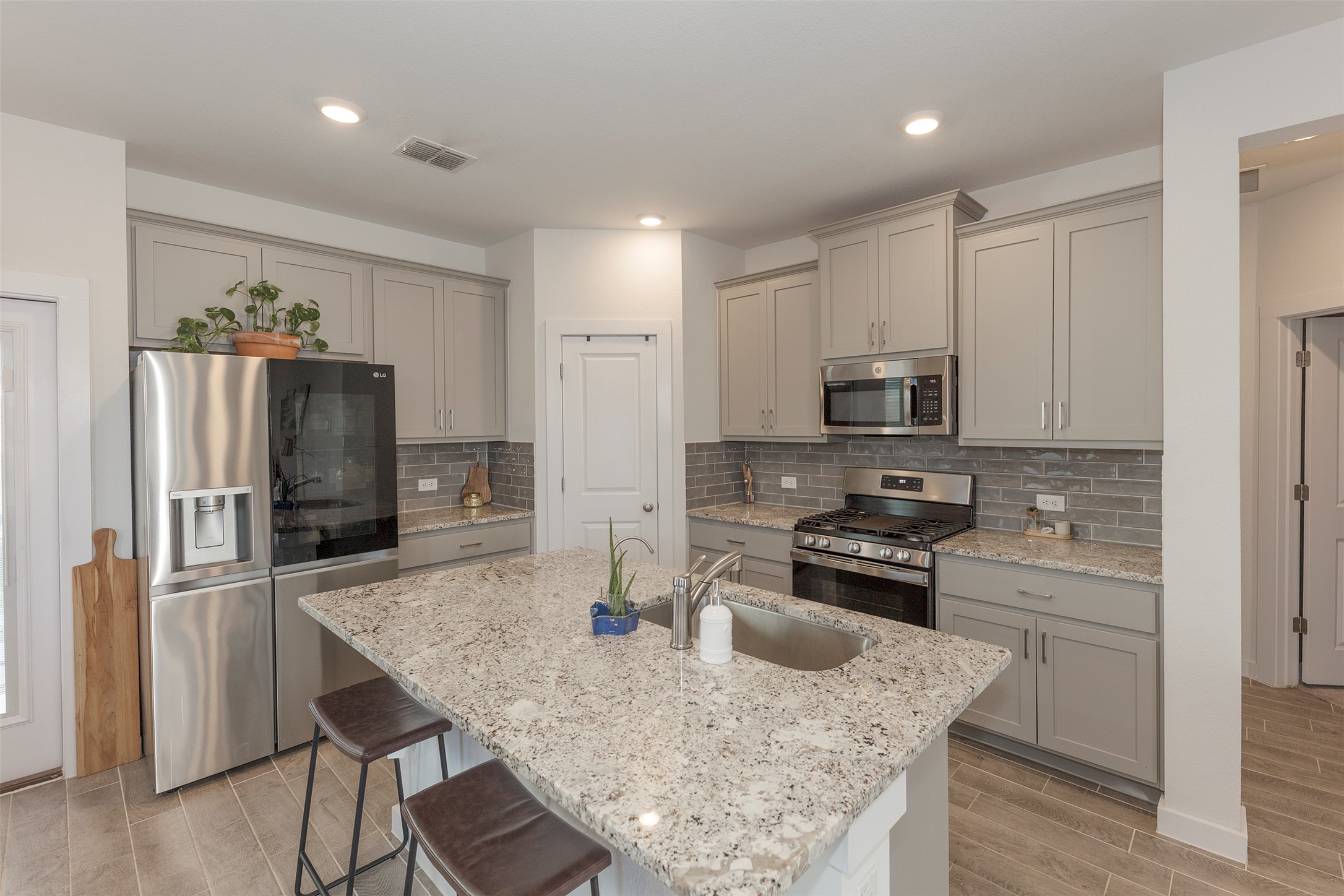 236 Garner Drive Kyle, TX 78640 - Photo 4 of 37 Kitchen with appliances with stainless steel finishes, wood tiled floors, light stone counters, gray cabinetry, and a breakfast bar