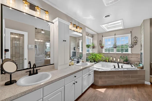 a bathroom with a double vanity sink a mirror a bathtub and next to a window