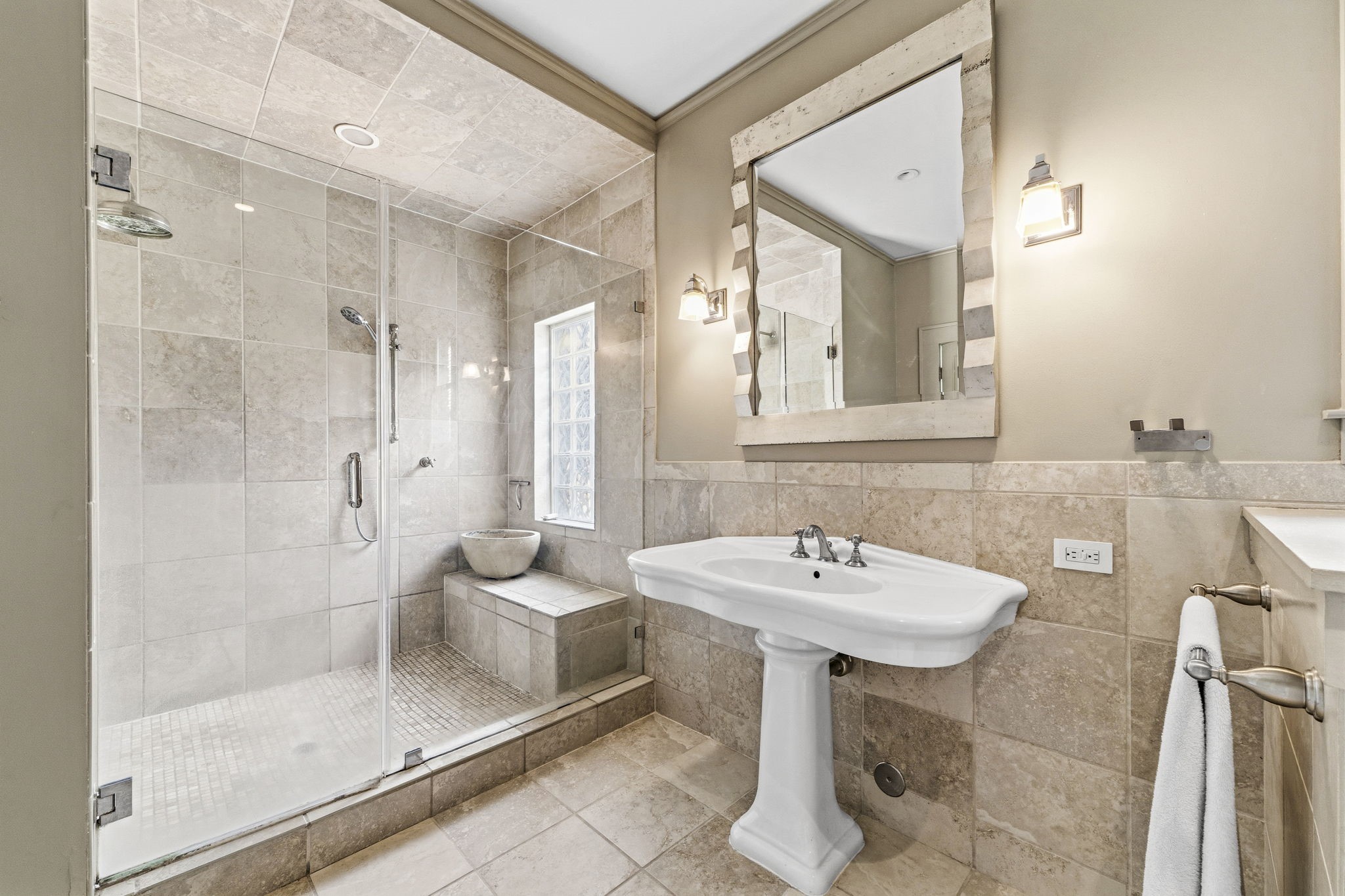 1521 Kipling Street Houston, TX 77006 - Photo 25 of 35 This bathroom features a spacious glass-enclosed shower with elegant tile work and a built-in bench. It has a modern pedestal sink, a large decorative mirror, and wall sconces for ambient lighting.
