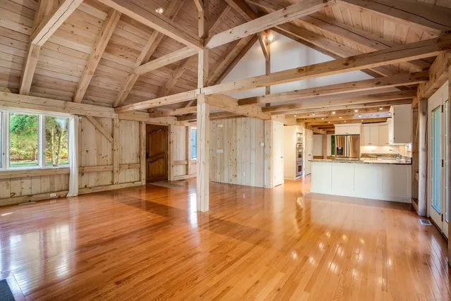 a view of an empty room with wooden floor and a kitchen