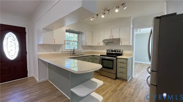 a kitchen with granite countertop a refrigerator a sink dishwasher a stove and white cabinets with wooden floor