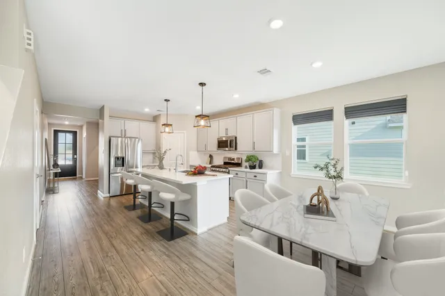 a open dining room with stainless steel appliances kitchen island granite countertop a stove a sink a refrigerator and white cabinets with wooden floor