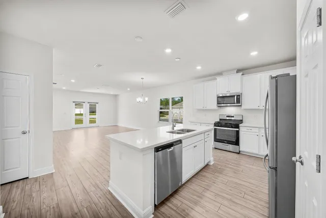 a kitchen with stainless steel appliances a sink a stove a refrigerator cabinets and wooden floor