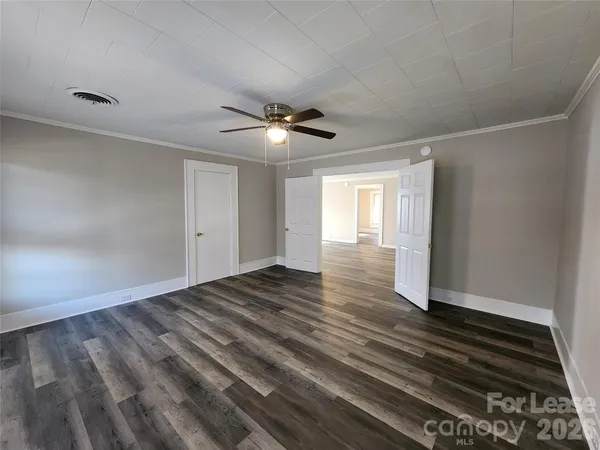 a view of an empty room with wooden floor and a ceiling fan